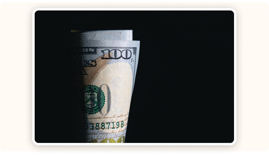 Rolled hundred dollar bills partially lit against dark background minimalist scene