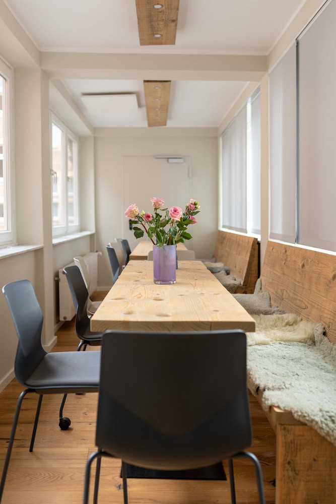 Heller Besprechungsraum bei SLB mit großem Holztisch, Stühlen und einem Blumenstrauß in der Mitte.