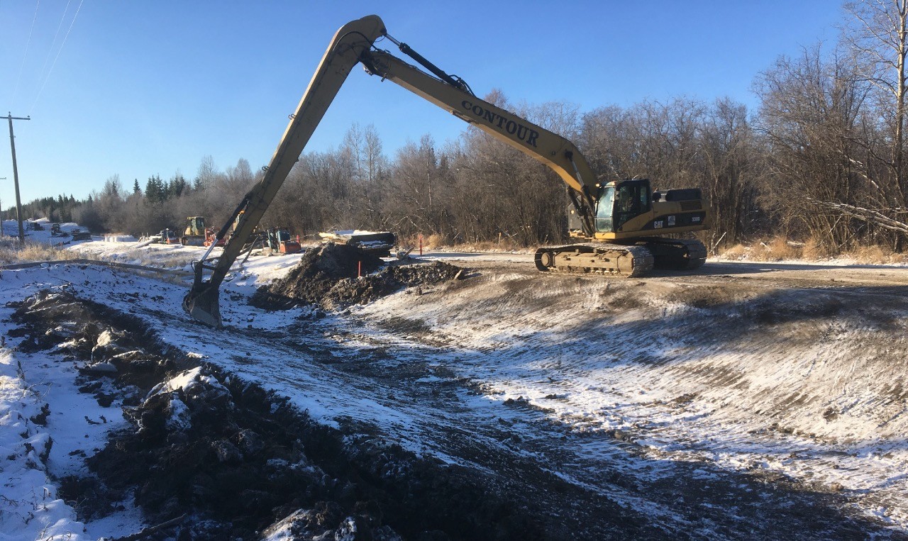 Long-reach excavator regrading a roadside ditch in winter at Carrot Creek Tower Road, Yellowhead County, Alberta
