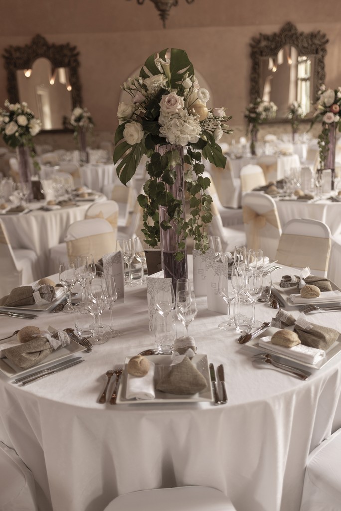 Luxury wedding reception setup with elegant floral centerpieces and fine tableware in a softly lit venue — refined editorial event styling. Décoration de réception de mariage de luxe avec centres de table floraux élégants et vaisselle raffinée dans une salle éclairée avec douceur — mise en scène éditoriale et raffinée.