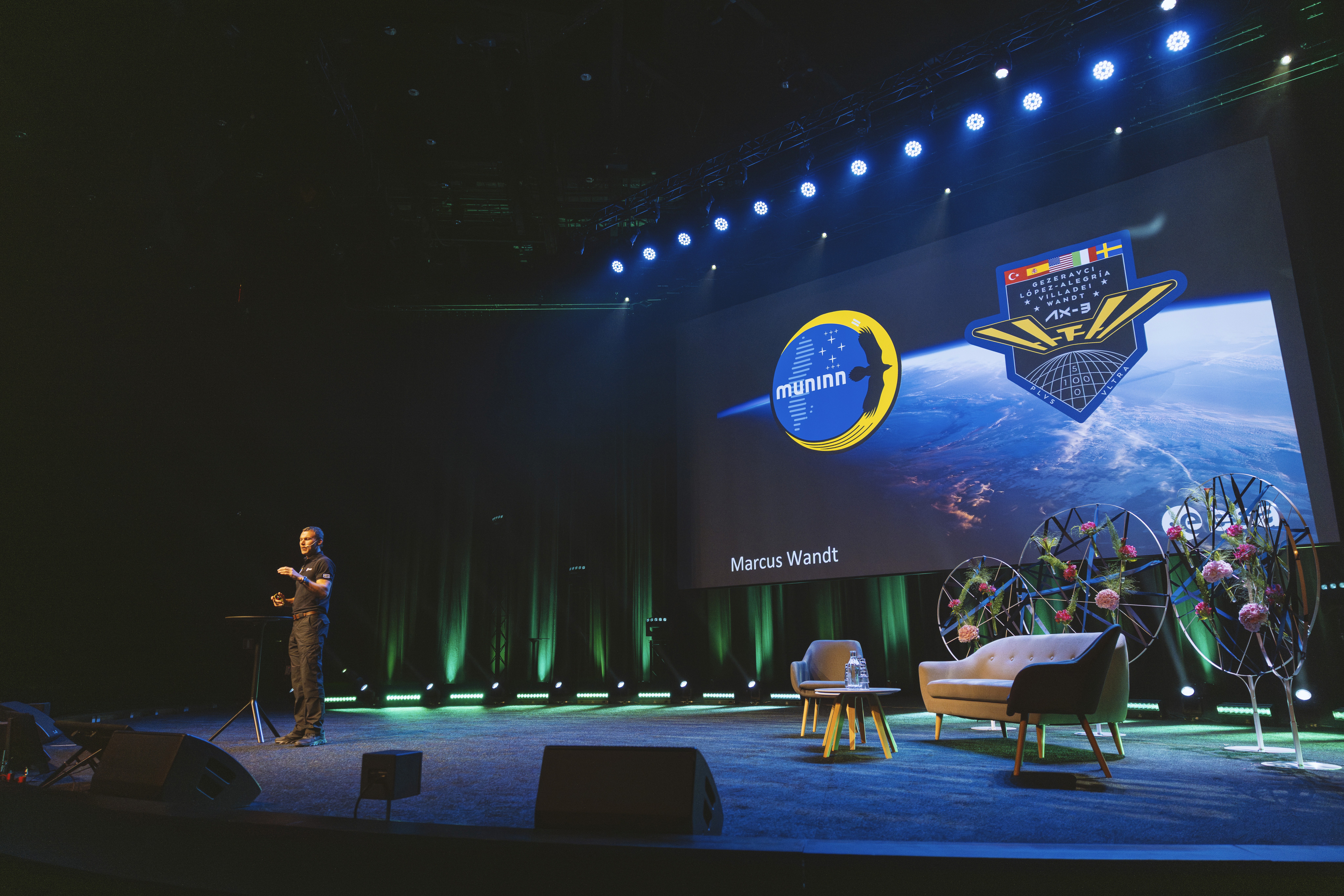 Presentatör talar på scen med rymdrelaterade bilder i bakgrunden