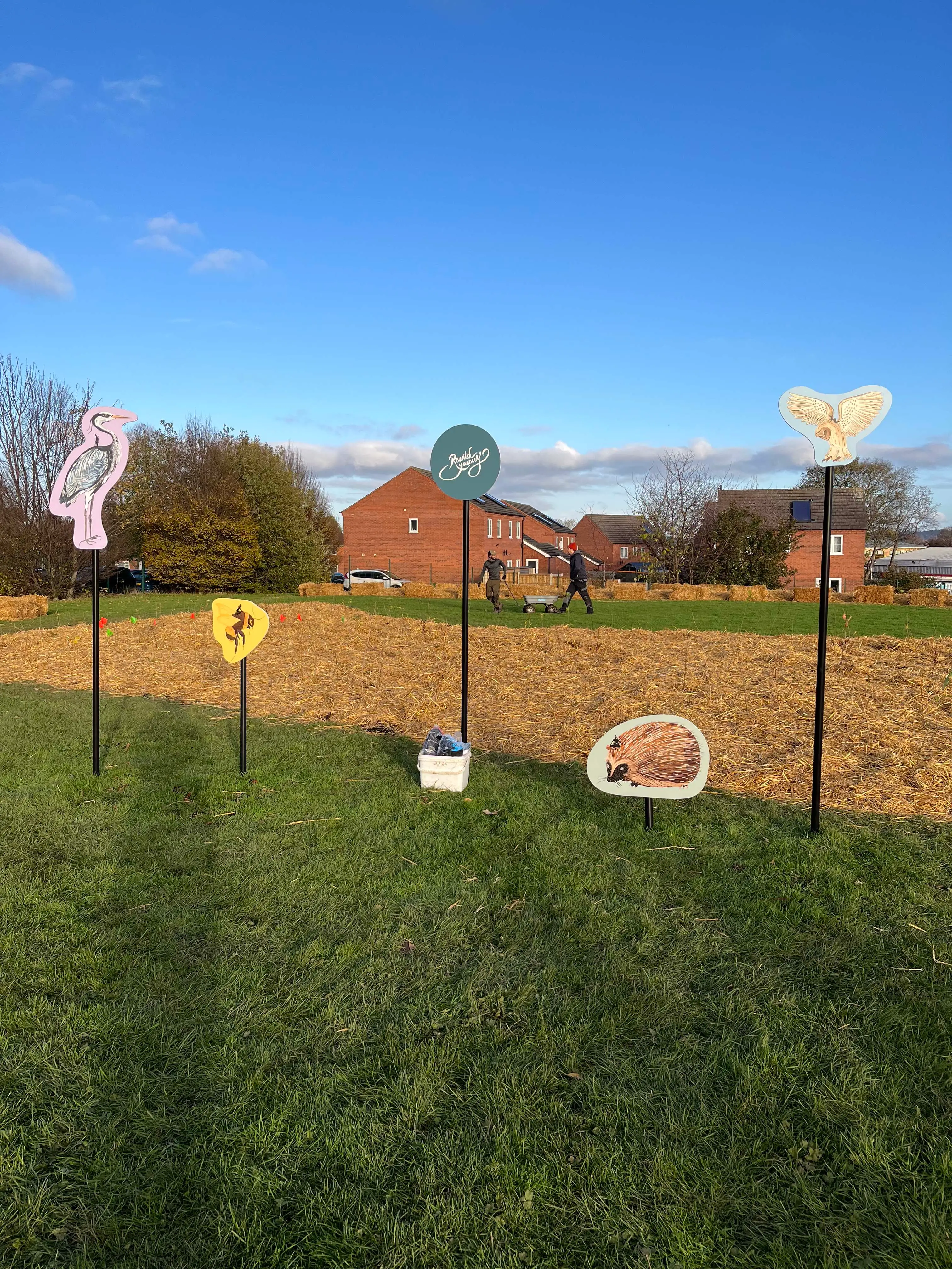 A grassy area with a fence, signs, and a clear blue sky in the background, featuring a building in the distance.