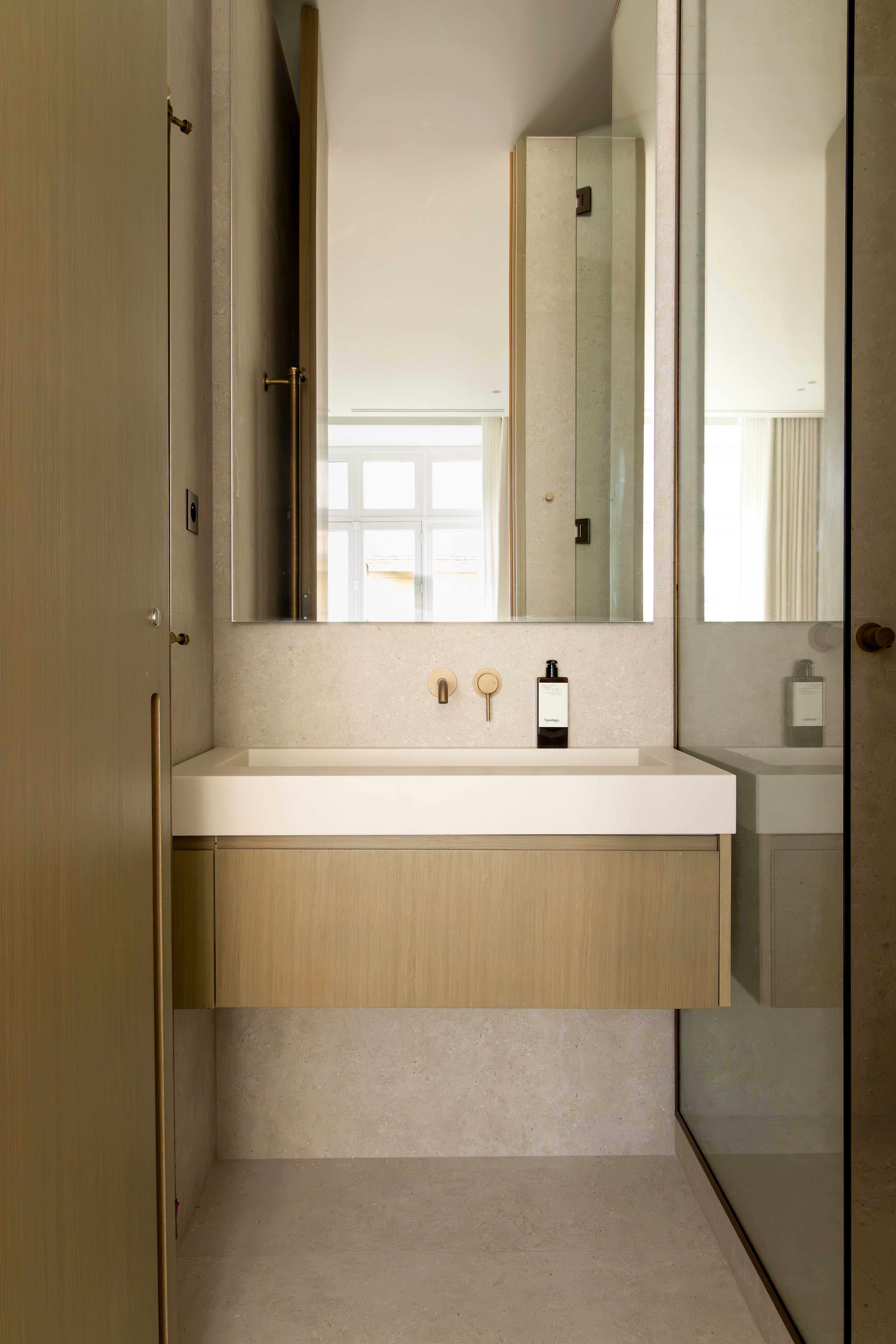 Vasque suspendue en bois clair avec robinetterie doree murale, grand miroir et paroi de douche en verre