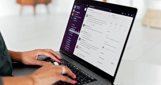 Mãos digitando num laptop que exibe uma interface de conversa, sobre uma mesa junto à janela