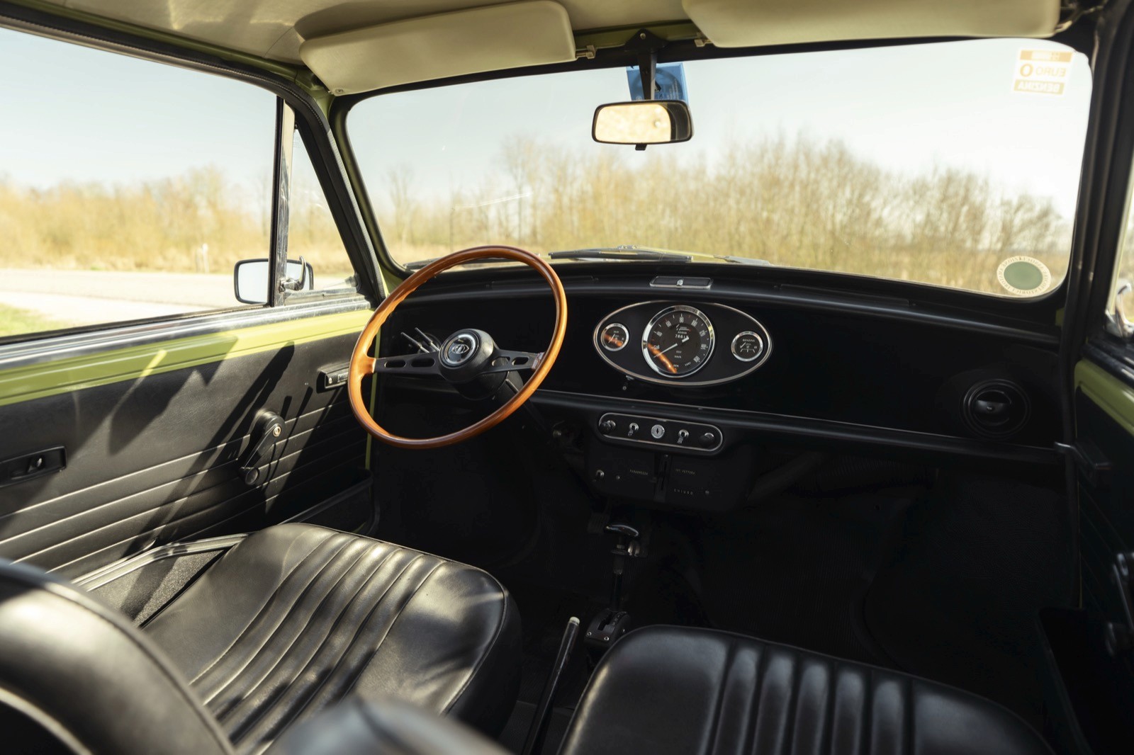 Interior view of a vehicle, featuring a wooden steering wheel and a dashboard with controls in a desert setting.