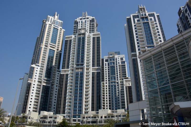 Dubai skyline featuring prominent high-rise towers against a clear blue sky, as seen from a wide street view.