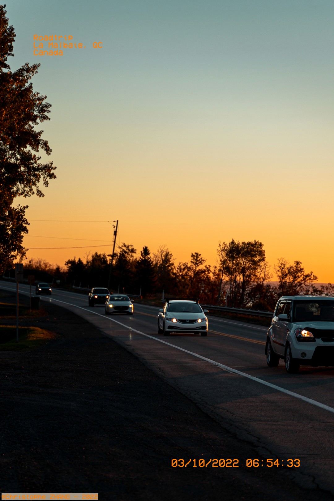 Trafic matinal à La Malbaie, avec le ciel orangé de l'aube en arrière-plan.