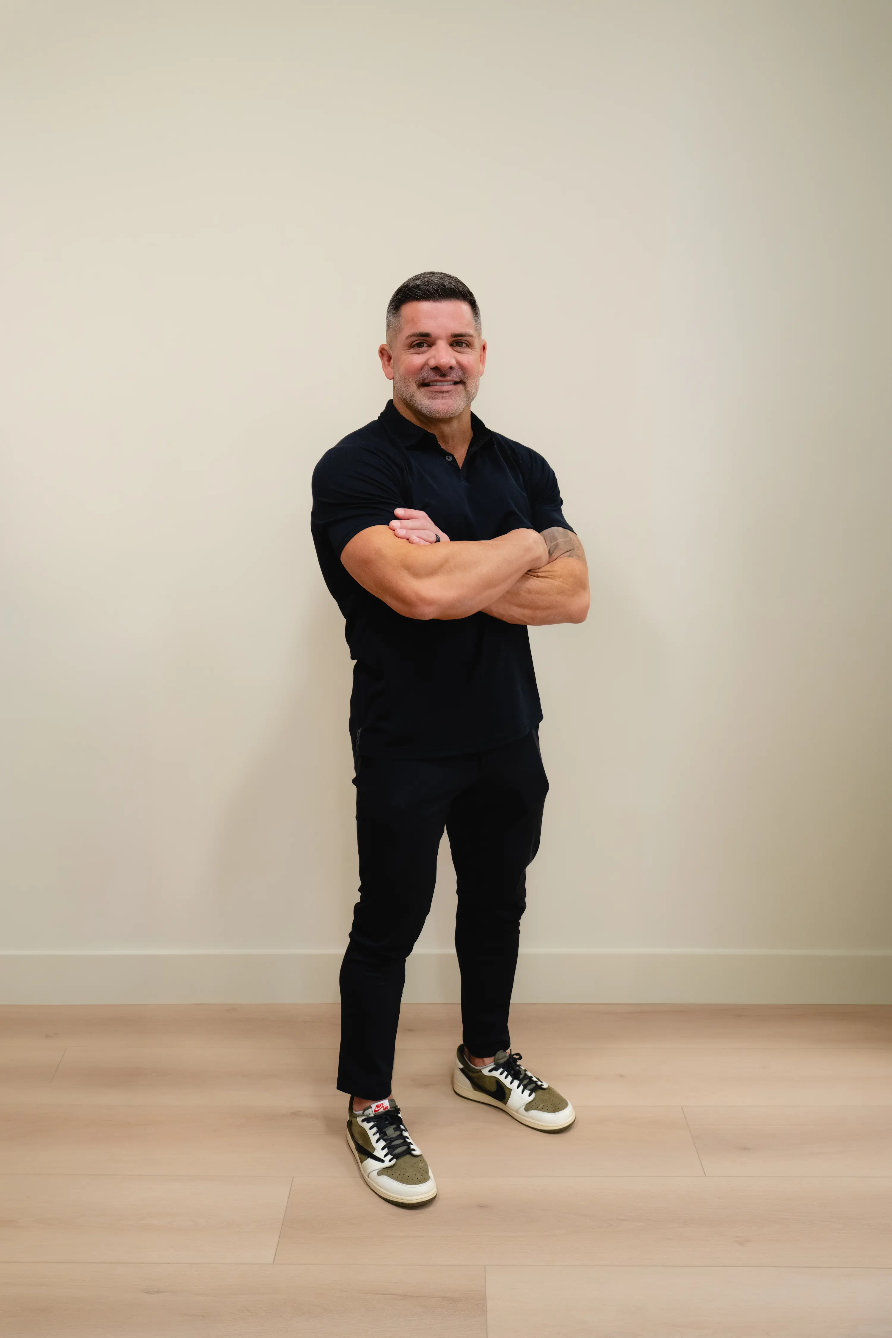 Man in black standing with arms crossed against a white wall