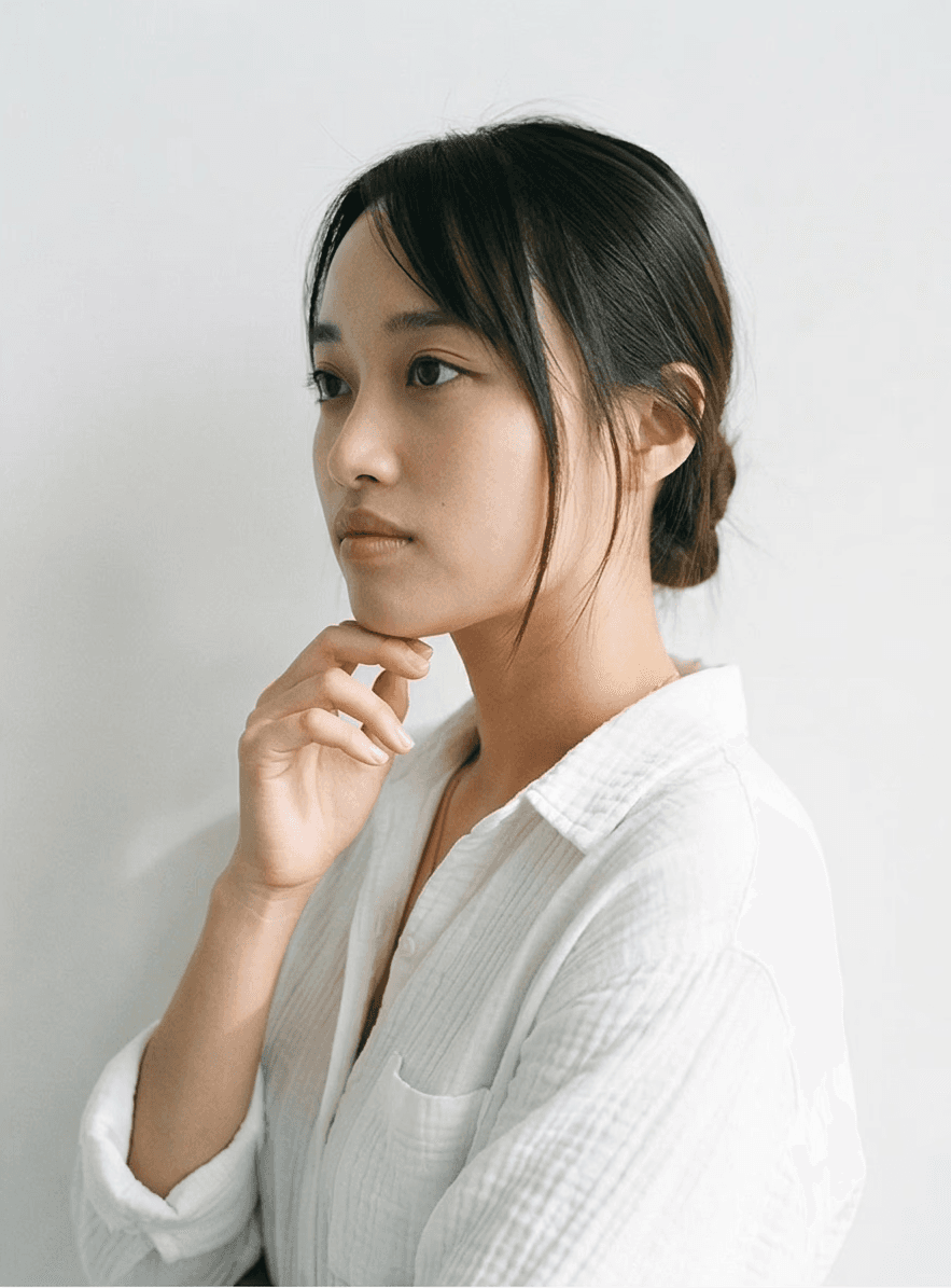 A thoughtful young person with dark hair gazes to the side, captured in soft black and white lighting.
