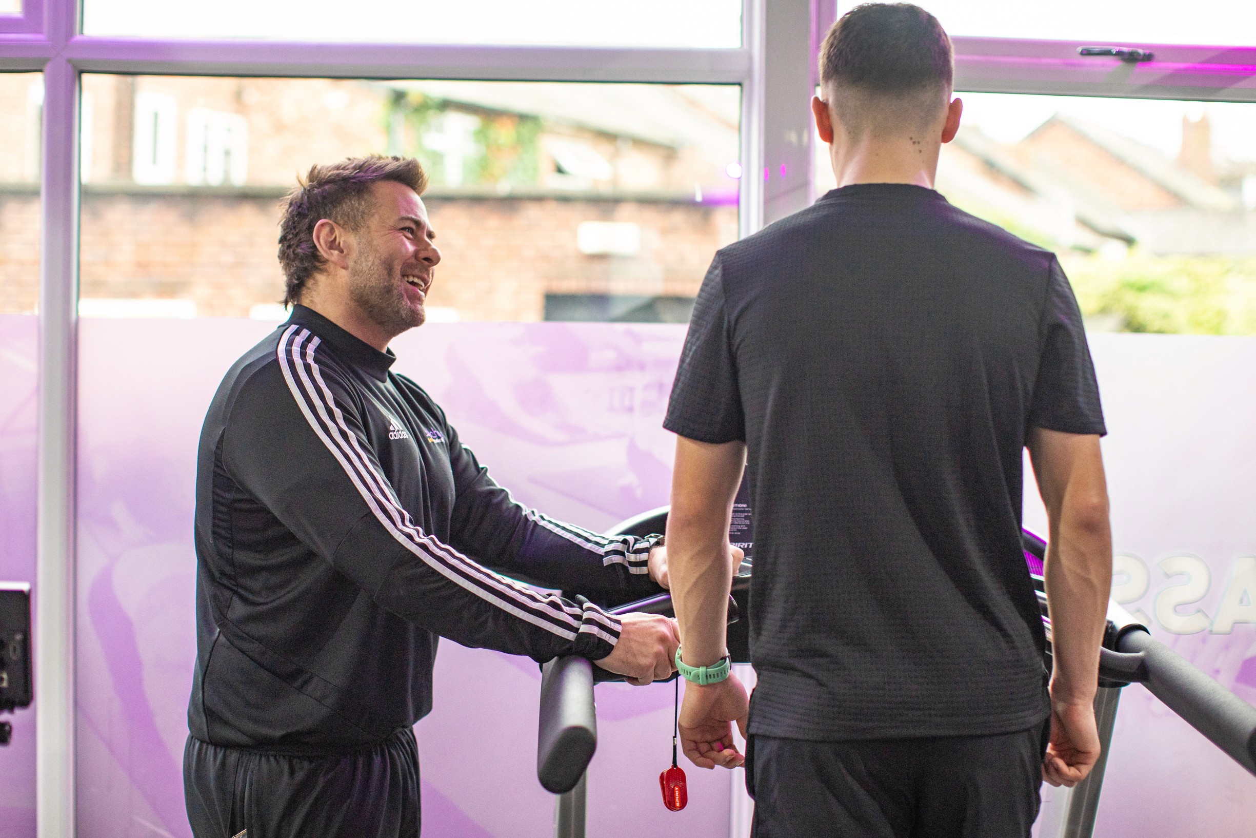 A personal coach is smiling with his arms crossed, wearing a black 