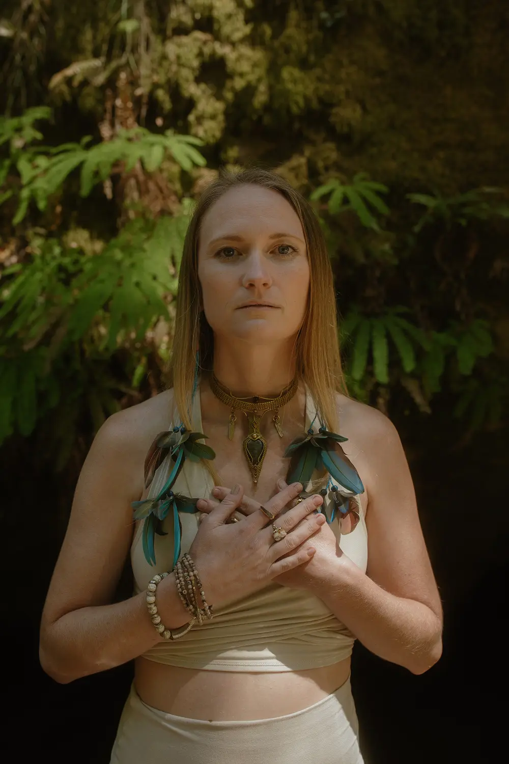 Emeline with hands on heart wearing a sacred feather adornment, representing devoted ceremonial presence