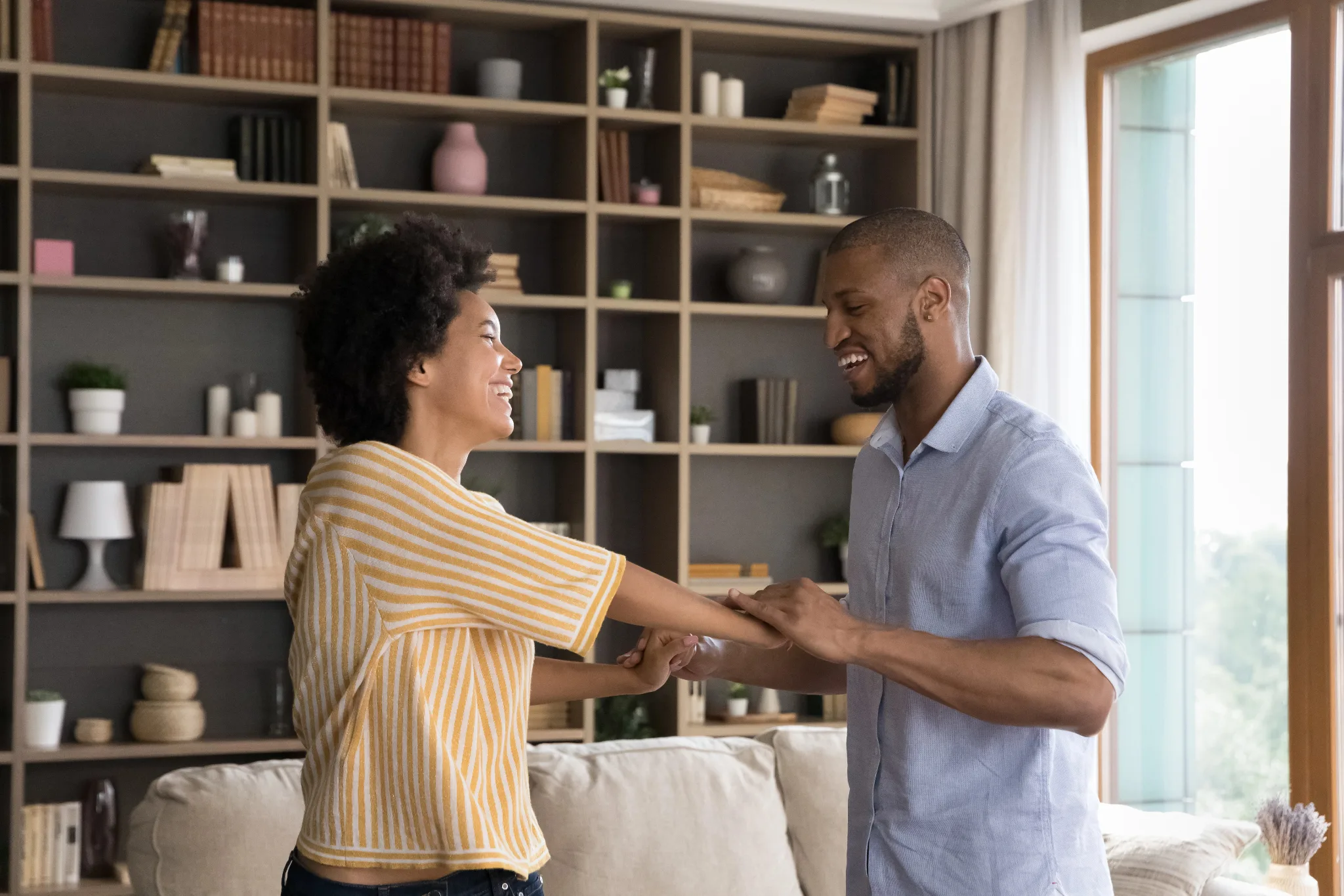 Happy black couple standing in a living room, holding both hands. celebrating 