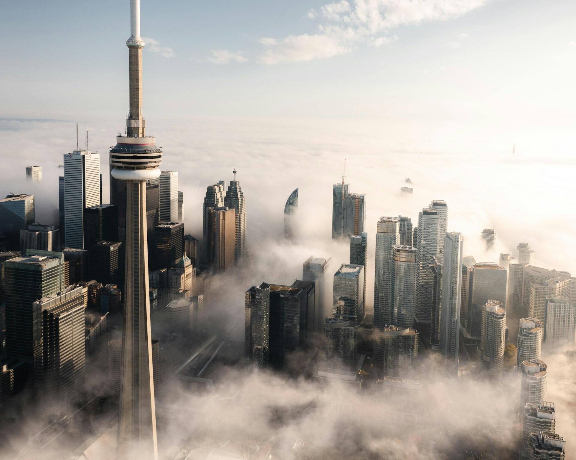 Aerial view of the CN Tower rising above skyscrapers partially wrapped in low cloud.