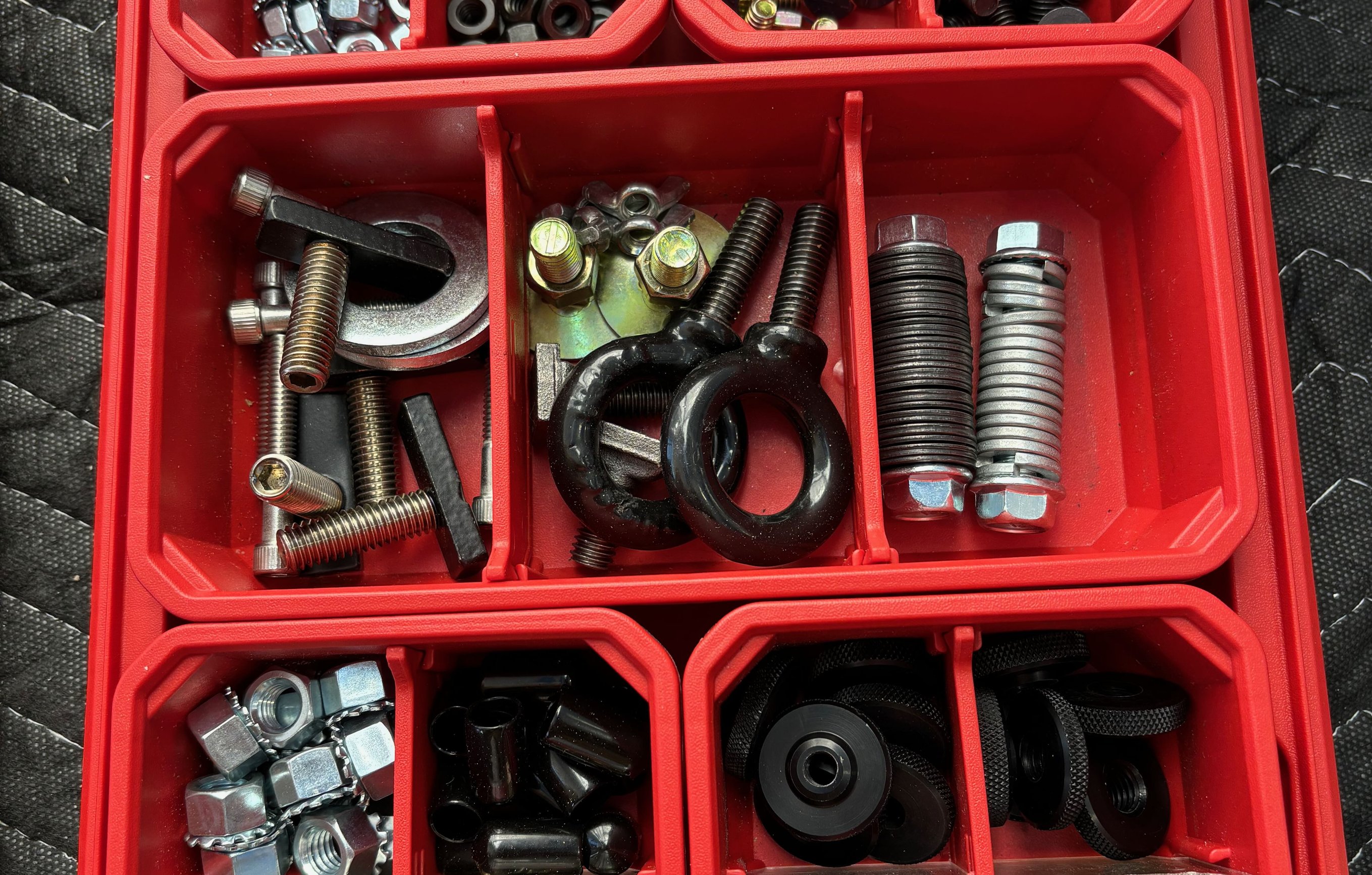 Red Milwaukee Packout organizer stocked with locking nuts, steel nuts, eye bolts, grub screws, and assorted fastening hardware