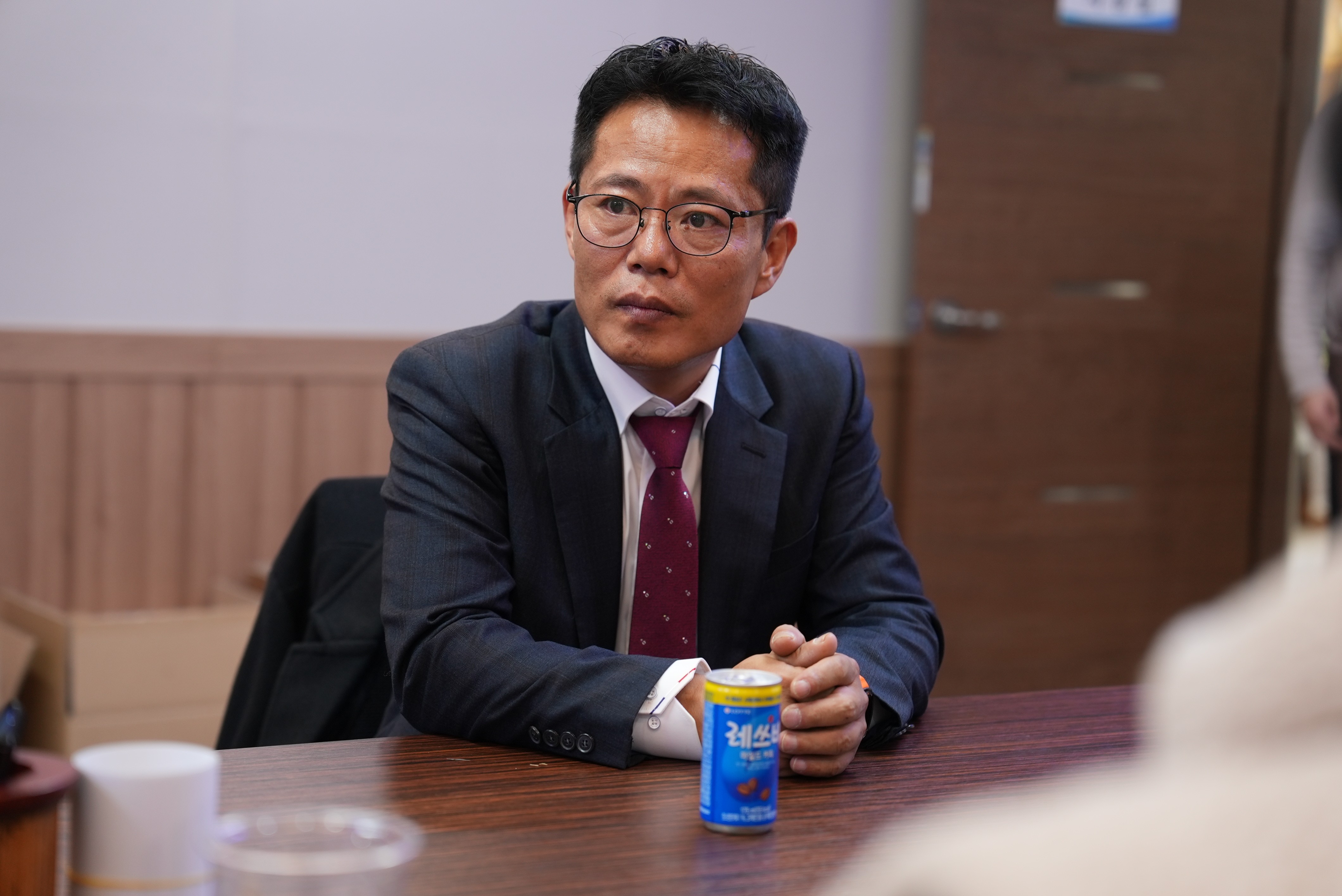 Modern open-concept living room with a large beige sectional, a wall-mounted TV, sleek barstools, wooden accents, and natural light from large windows. Cozy atmosphere.