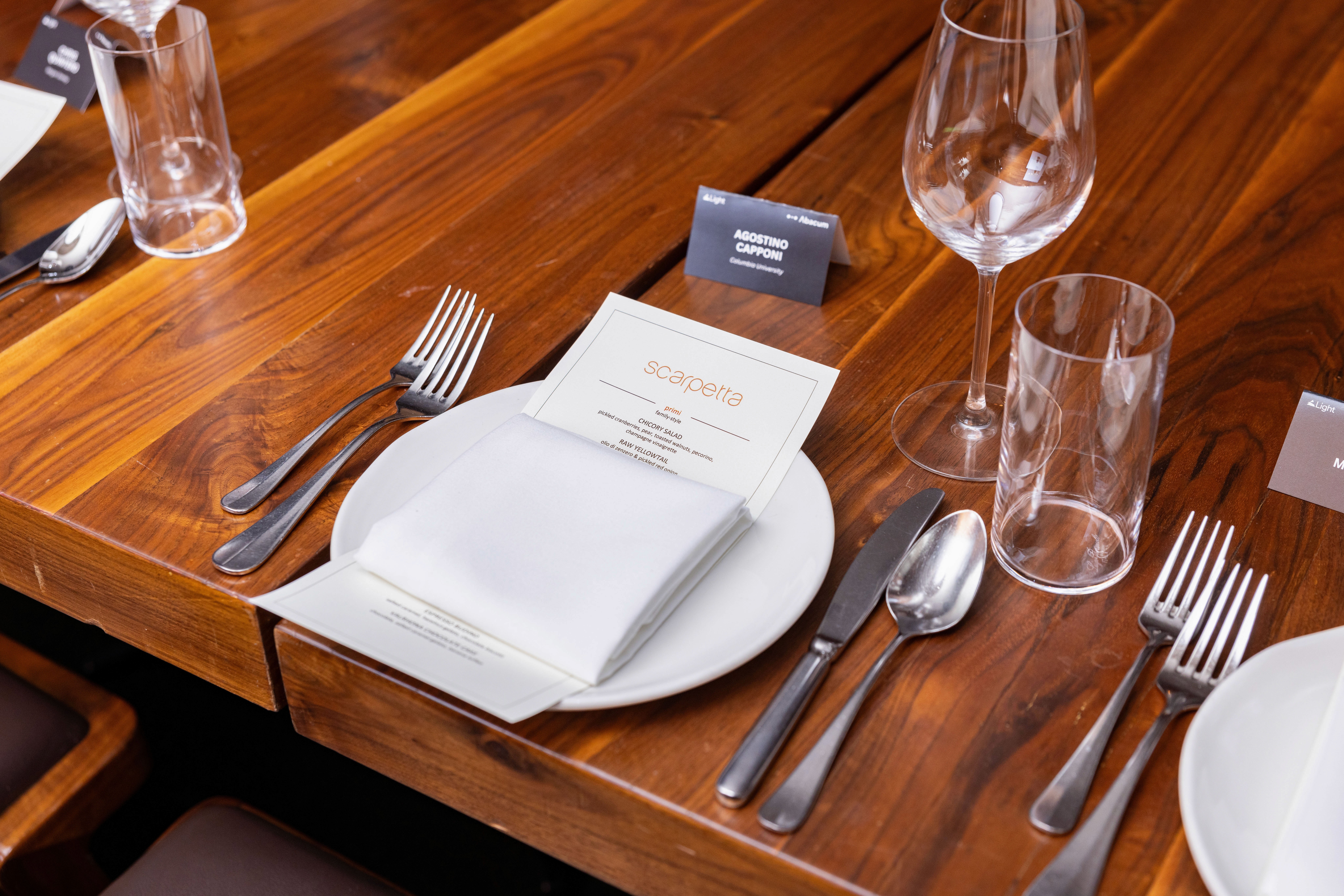 A neatly set dining table with a white plate, folded napkin, utensils, and glassware on a wooden surface.