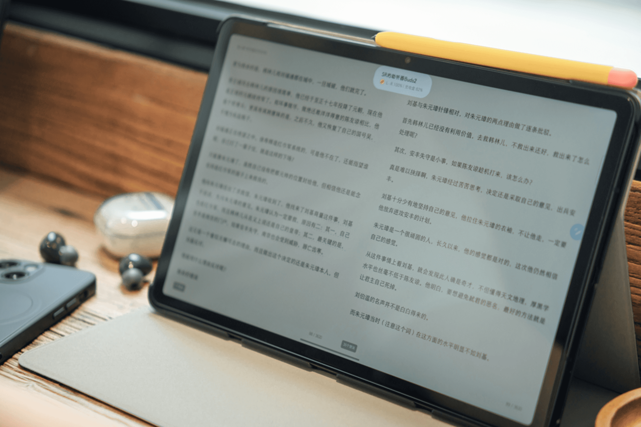 Tablet displaying a document on a desk beside wireless earbuds and a smartphone.