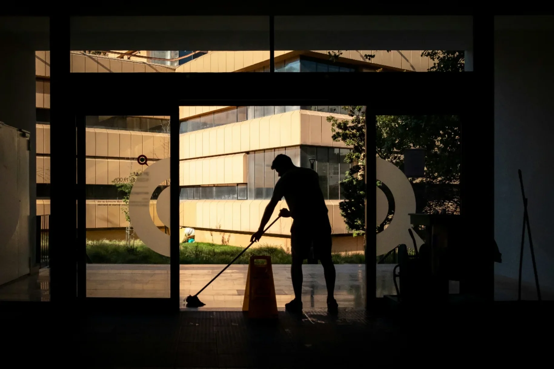 Im Hintergrund ist die Silhouette einer Person beim Wischen vor einer großen Fensterfront zu sehen