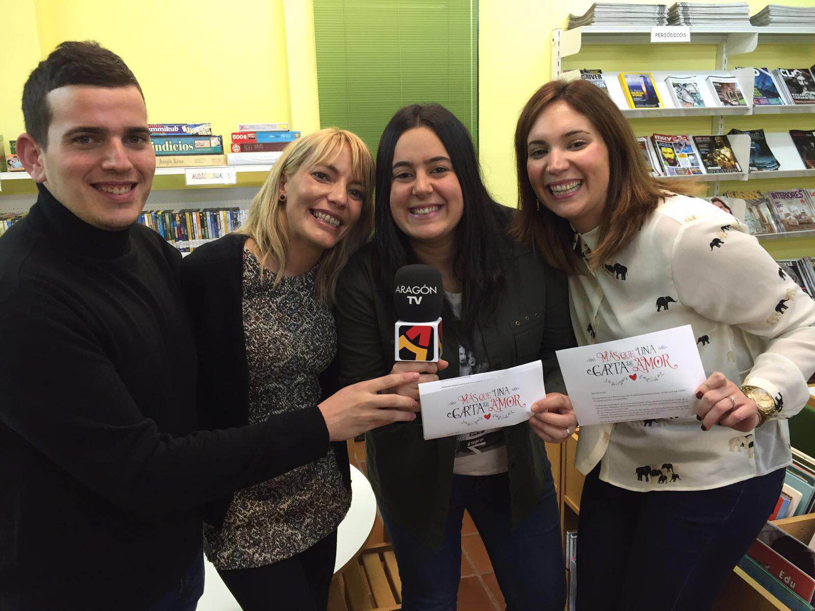 Grupo de personas sonriendo sosteniendo cartas en una biblioteca.