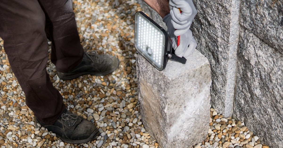 Installer adjusts an outdoor lighting fixture beside a stone wall to achieve the intended placement and lighting effect.