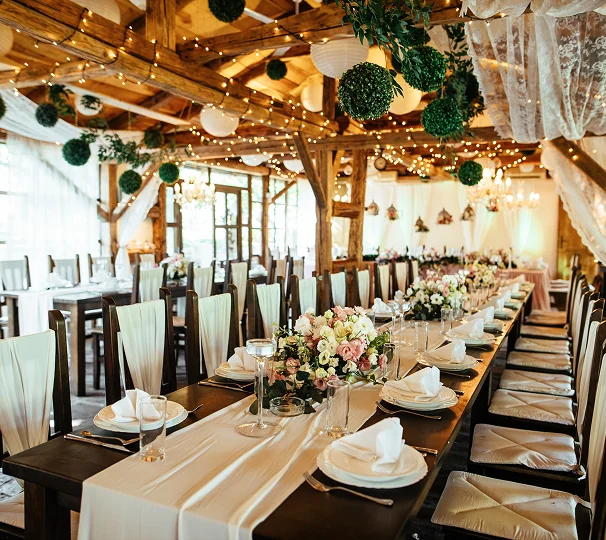 alt="Свадебный банкет с длинными столами, пастельными цветами и подвесным декором в зале с балками