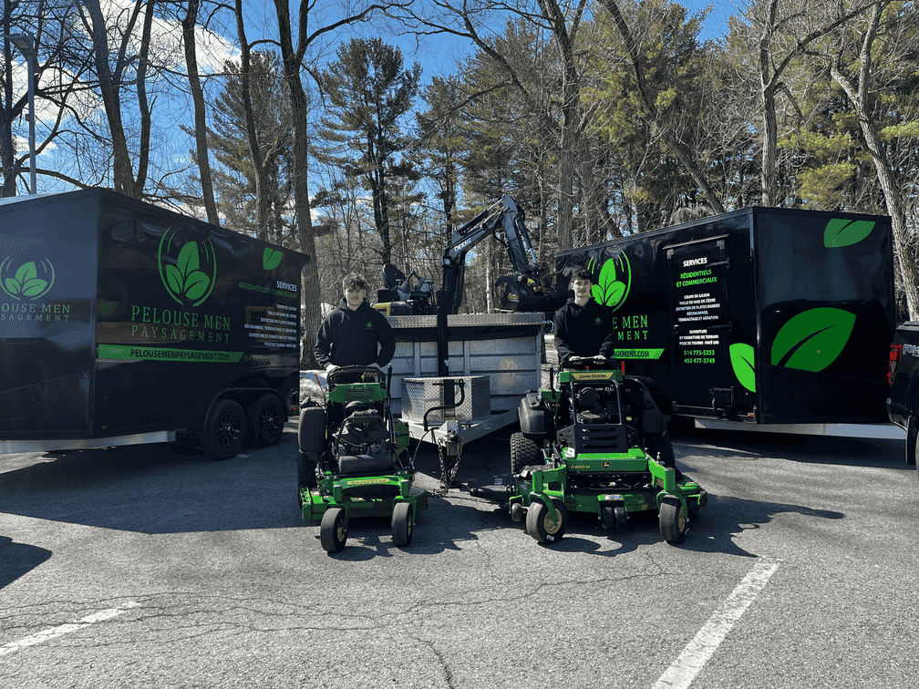 Deux tondeuses vertes de Pelouse Men Paysagement stationnées devant les camions noirs de l’entreprise de paysagement.