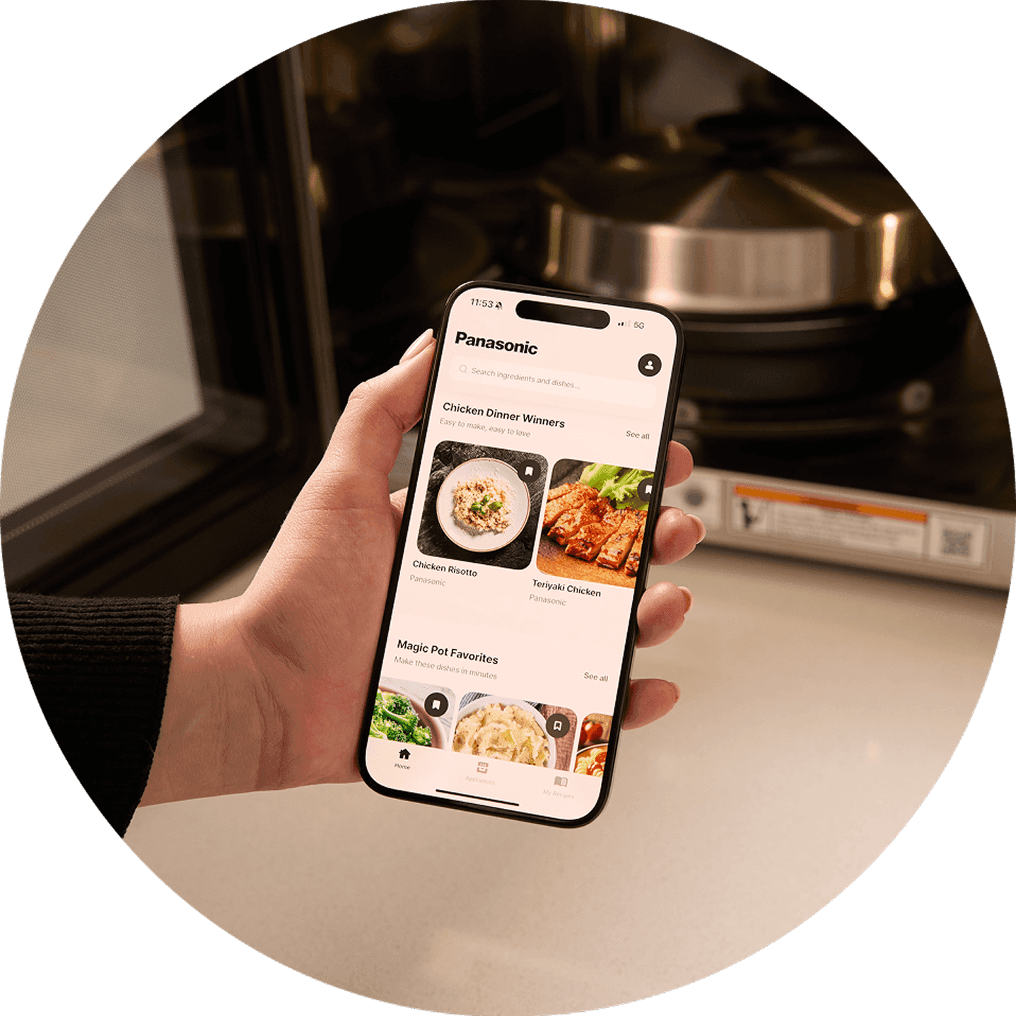 A hand holds a smartphone displaying a food ordering app, with a kitchen background visible.