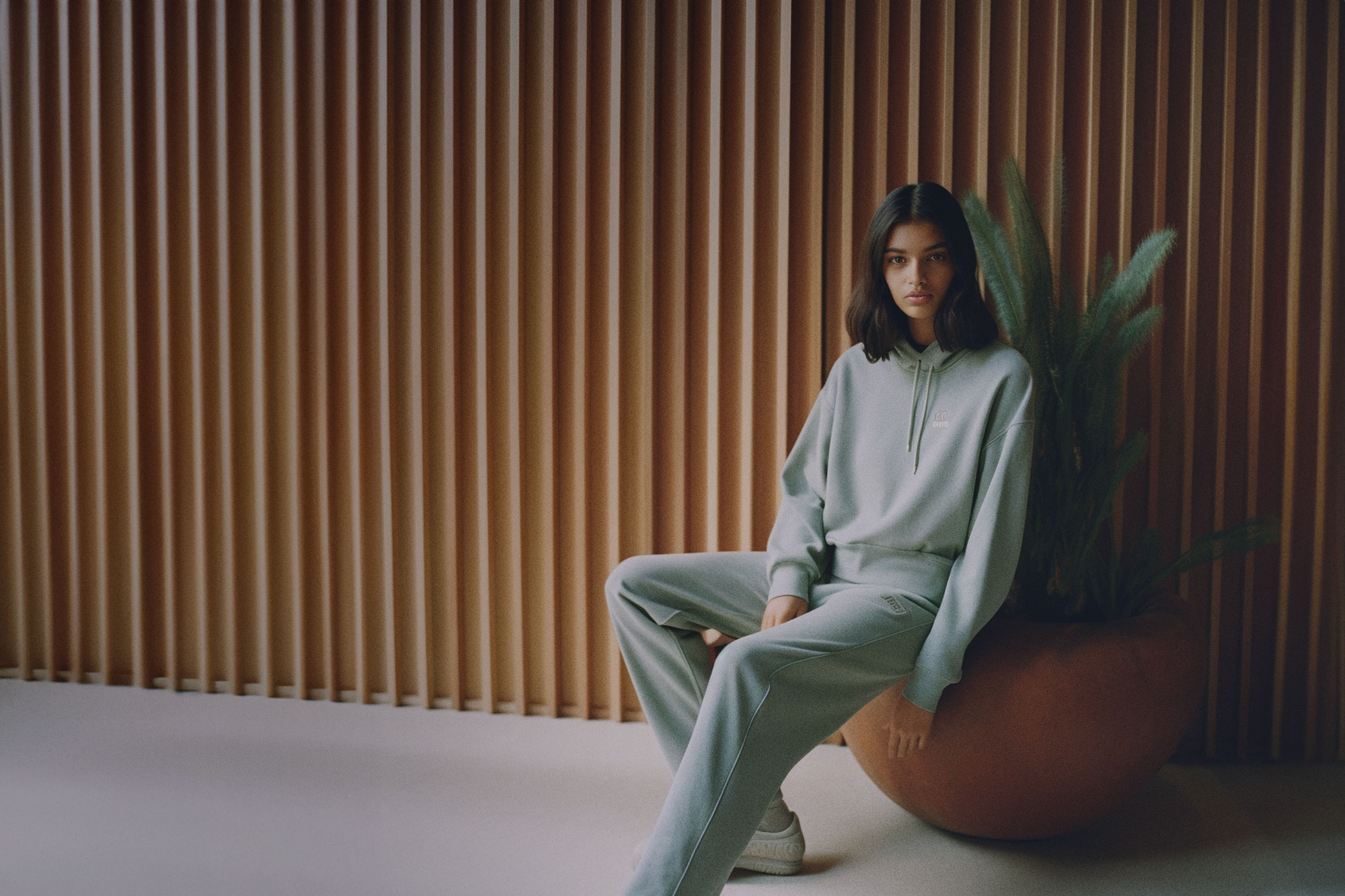Woman in sweatsuit sitting on plant against wood wall