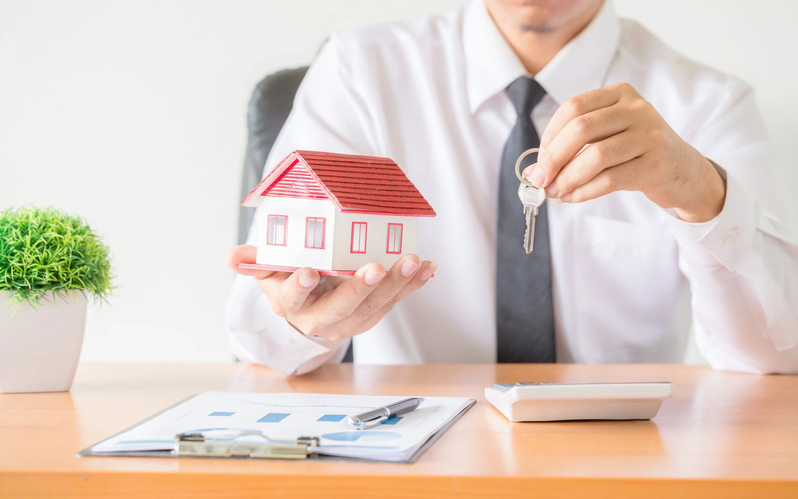 Male hole house keys in one hand and a small house in the other.
