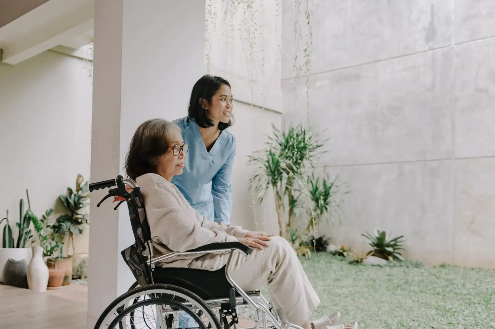 Pflegerin mit Seniorin im Rollstuhl in hellem Raum – Symbolbild für Elderly Care als attraktive Investitionsnische