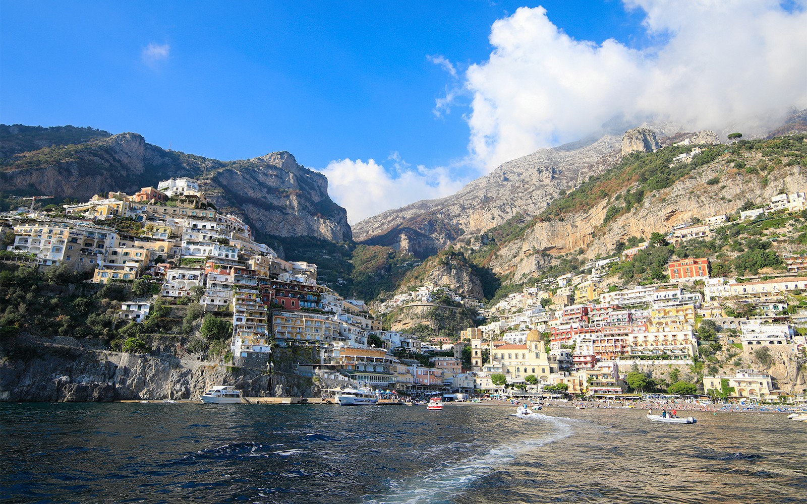 Amalfikusten sedd från havet med färgglada byggnader på klippor och båtar i Positano, Italien.