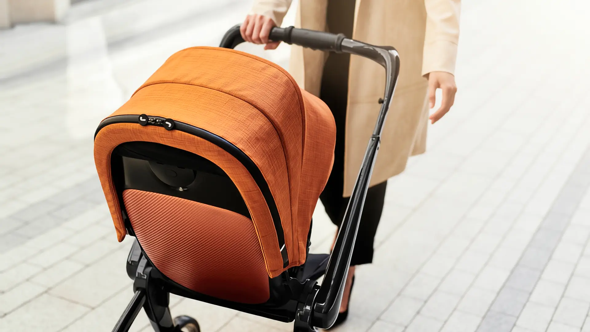 Rear view of a JUNIORJONES stroller with rust-coloured fabric being pushed outdoors by an adult.