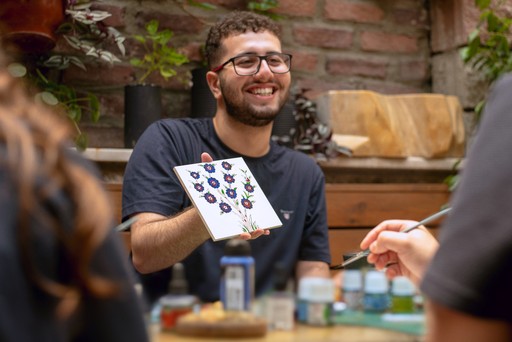 A participant smiling while painting tiles at a Turkish tile art workshop in Istanbul. This interactive ceramic workshop is a popular attraction in Istanbul, ideal for creative travelers.