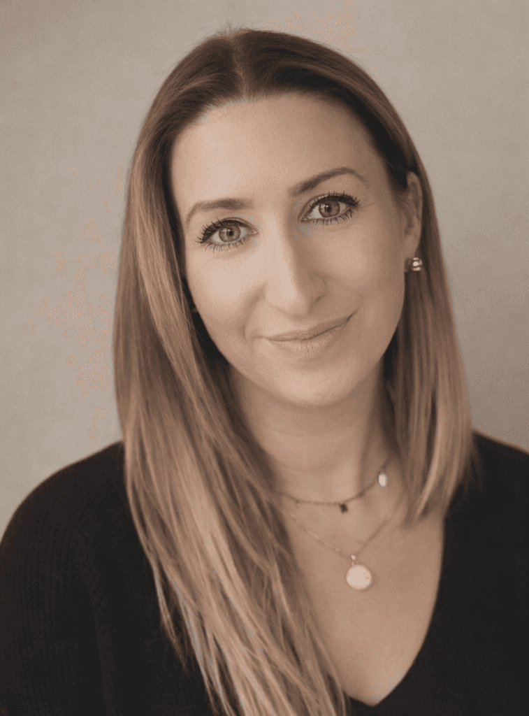 A person with shoulder-length blonde hair wearing a black newsboy cap and a black sweater.