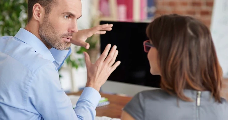 Homem e mulher conversando frente a frente numa mesa, ele gesticulando com as mãos