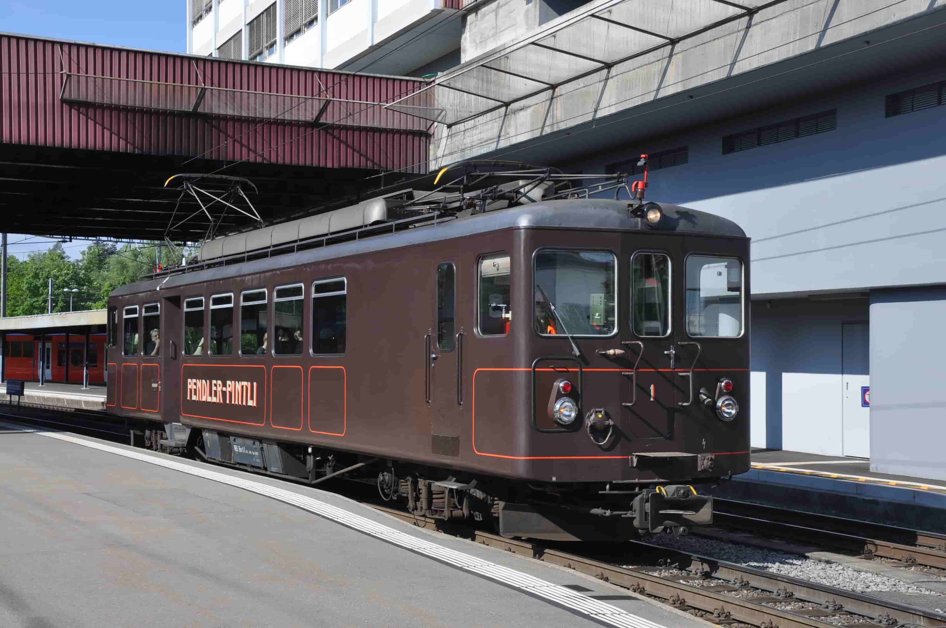 Der braune Triebzug Pendler Pintli an einem Bahnhofperron vom RBS