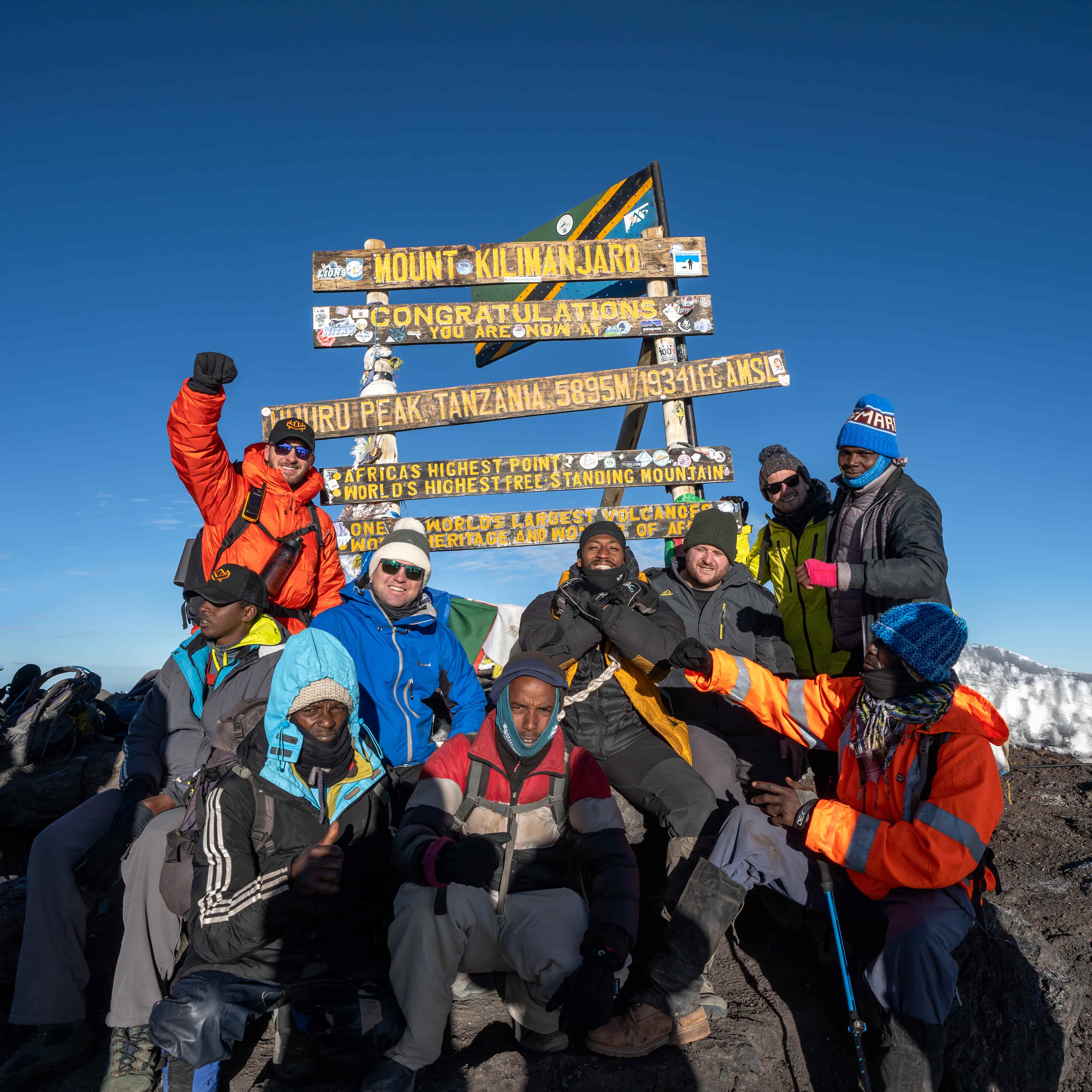 Legend Expeditions team celebrating at the Uhuru Peak summit sign after a successful Kilimanjaro climb.
