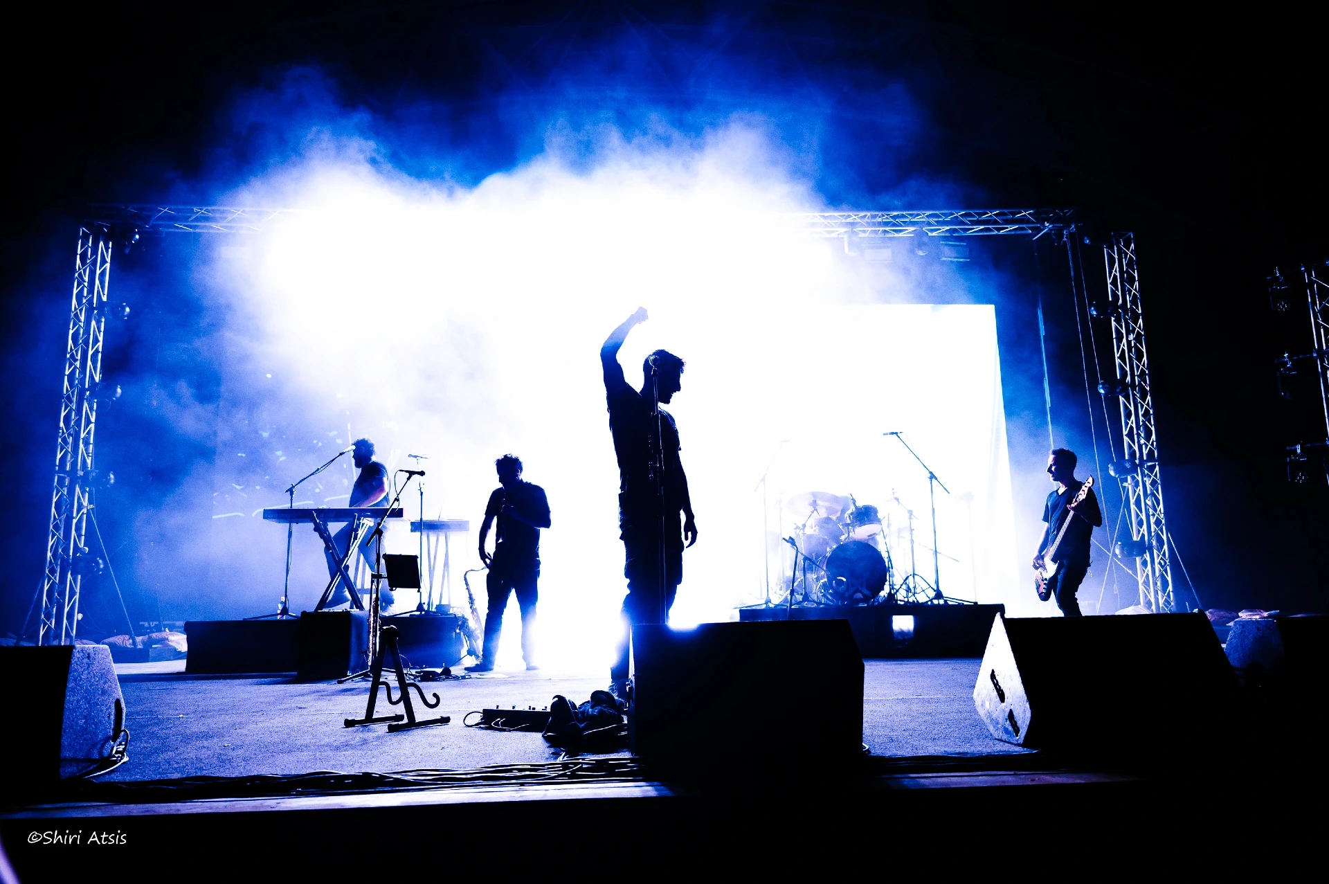 צילום הופעה חיה של עידן עמדי והלהקה על הבמה. צללית של האמן מול תאורה לבנה עוצמתית וערפל, יוצרים קומפוזיציה דרמטית ומלאת אנרגיה. צילום הופעות מקצועי מאת הצלמת שירי עציץ Shiriz Photography.