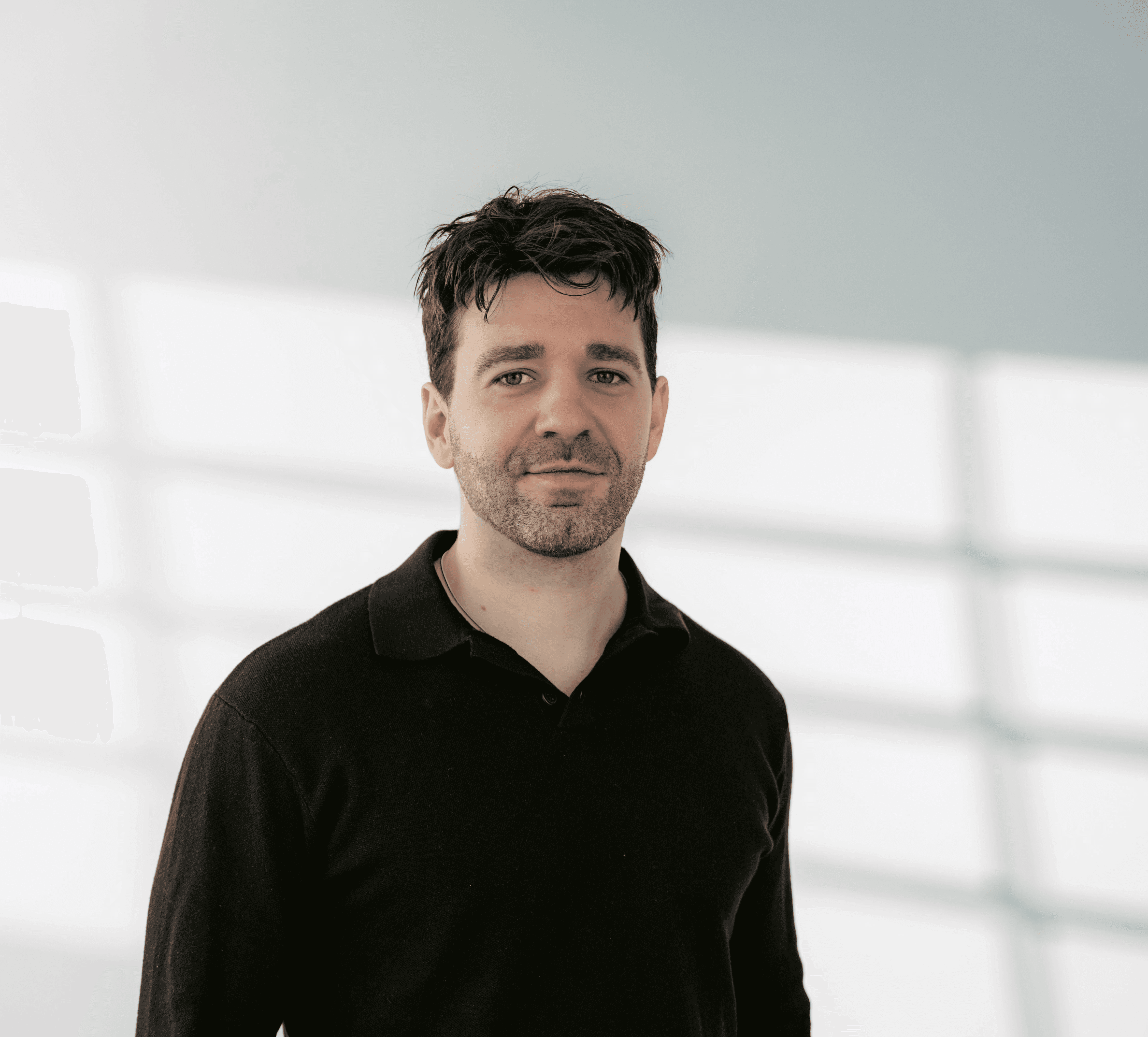 Ein Junger Mann mit schwarzem Pulllover und Hände in der Tasche blickt freundlich in die Kamera.