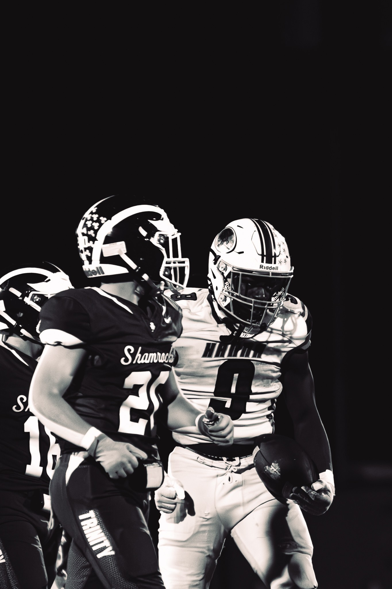 Black-and-white photograph of helmeted football players in contrasting uniforms standing close together.