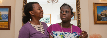Woman comforting young girl indoors, standing close together.