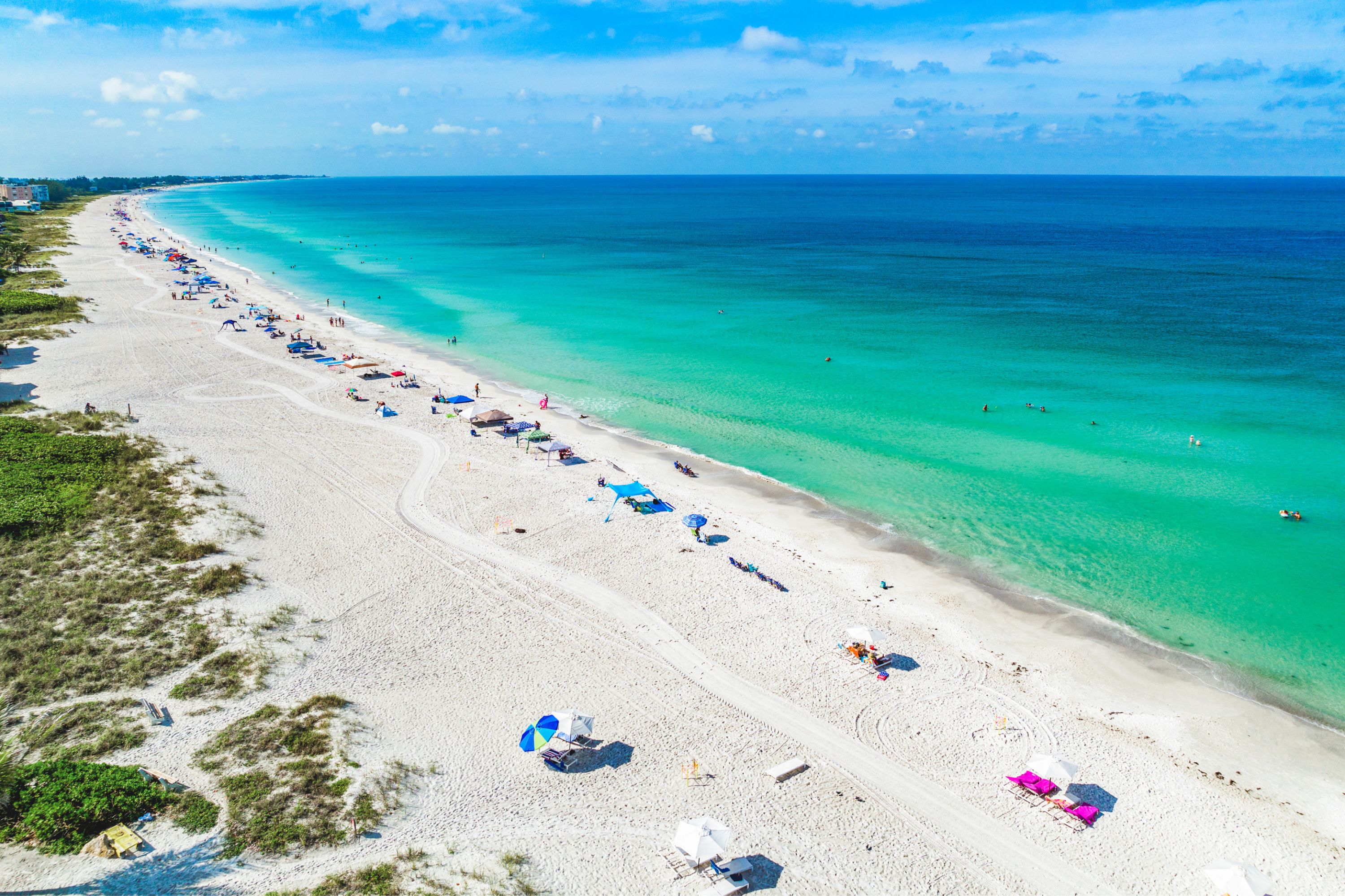 Aerial view of a white-sand Gulf Coast beach with turquoise water and scattered umbrellas near Bradenton and Sarasota