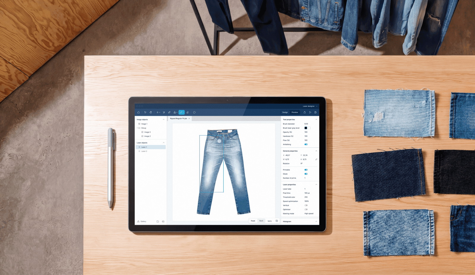 Workspace of a denim designer with a tablet computer showing the design software on a table, together with denim samples and garments