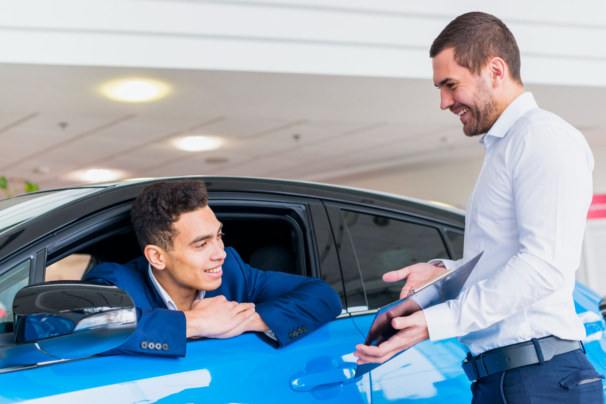 Inside a car dealership, a man discusses options with another man, showcasing the environment filled with cars for sale.