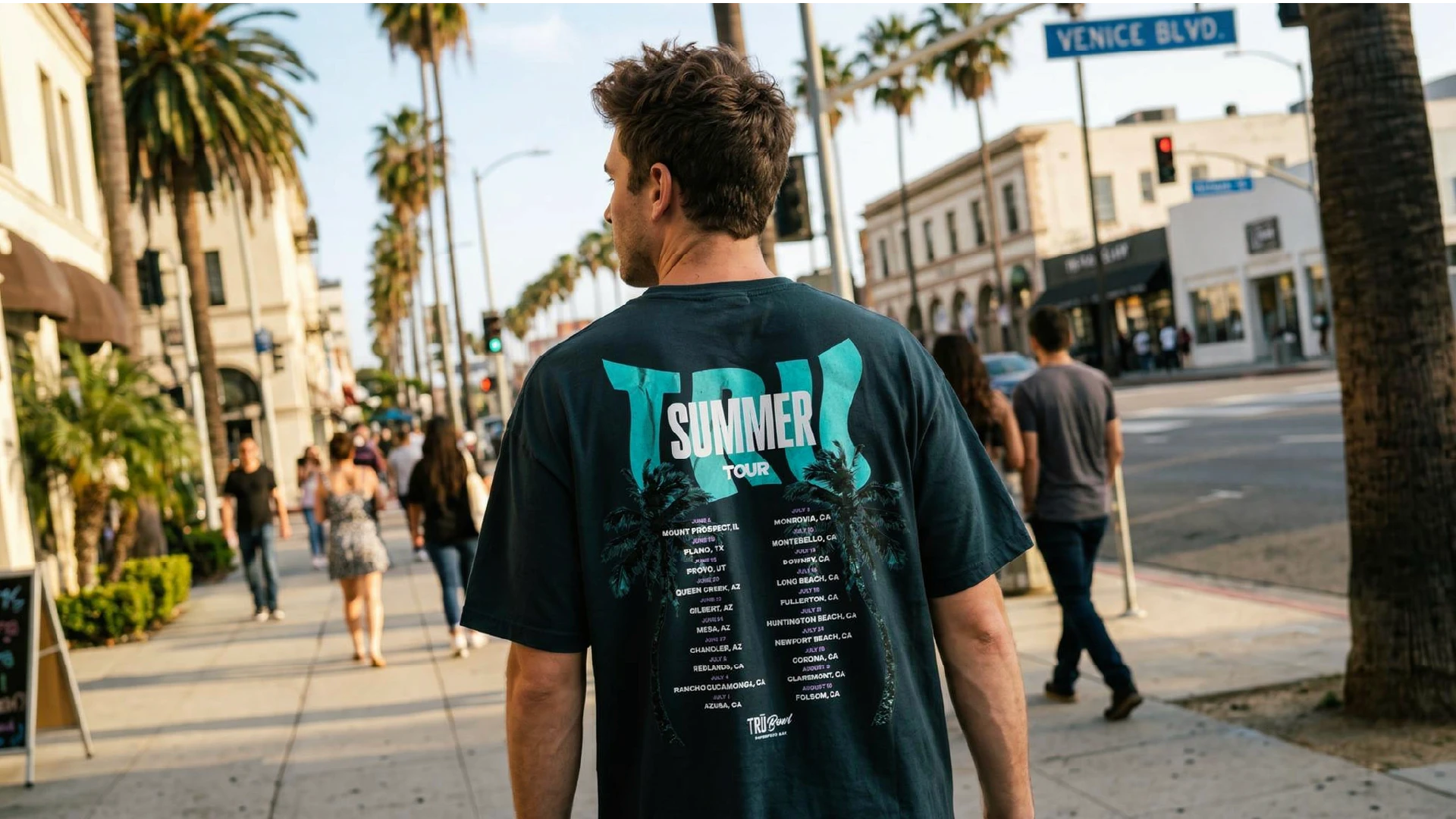 A man walking down the street showing off his t-shirt design. The design features palm trees, and the words 'TRU Summer Tour'