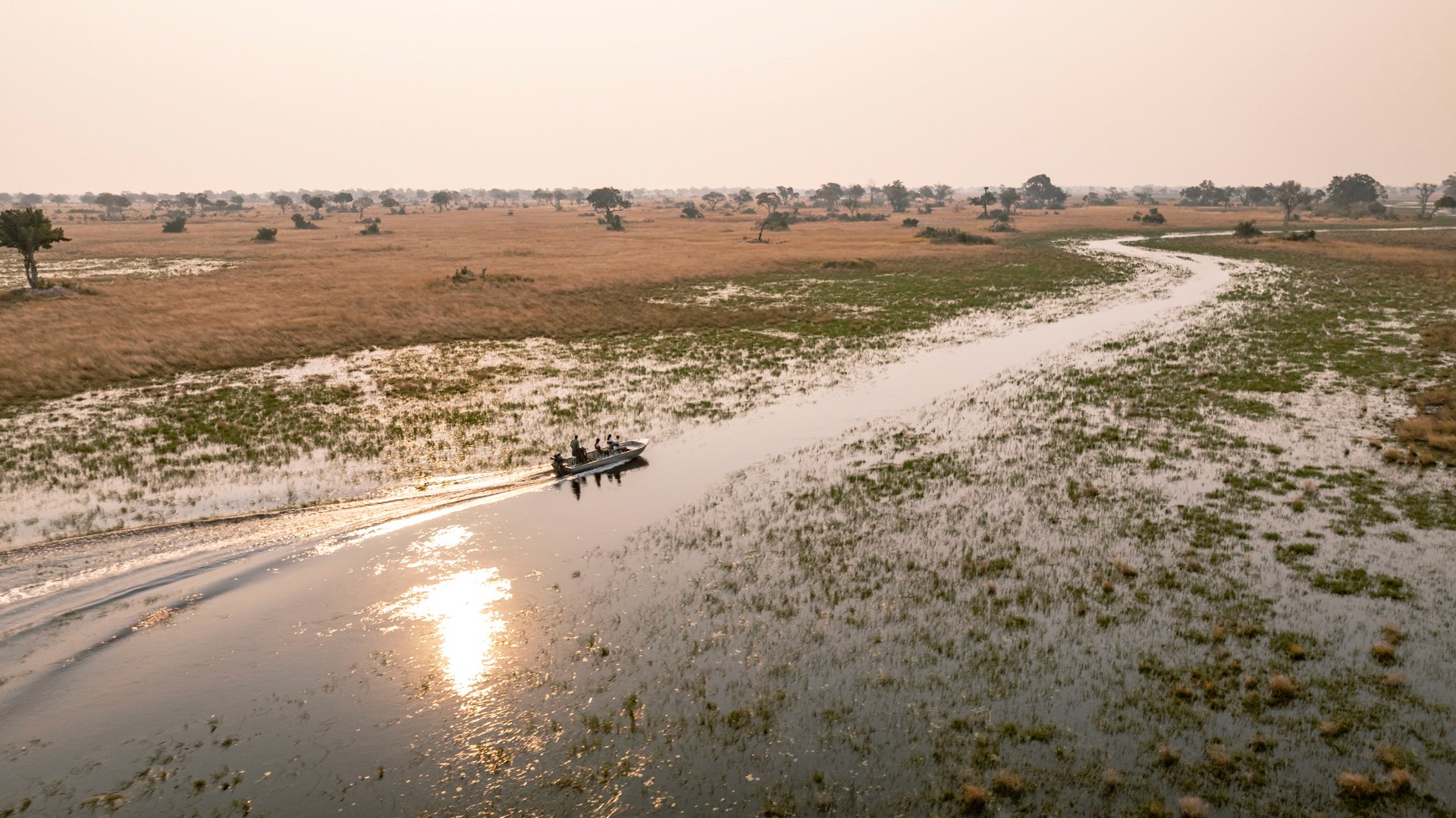 Kujwana Delta Ride, Okavango Delta, Botswana. En båt glider fram över en av deltats kanaler i solnedgången.