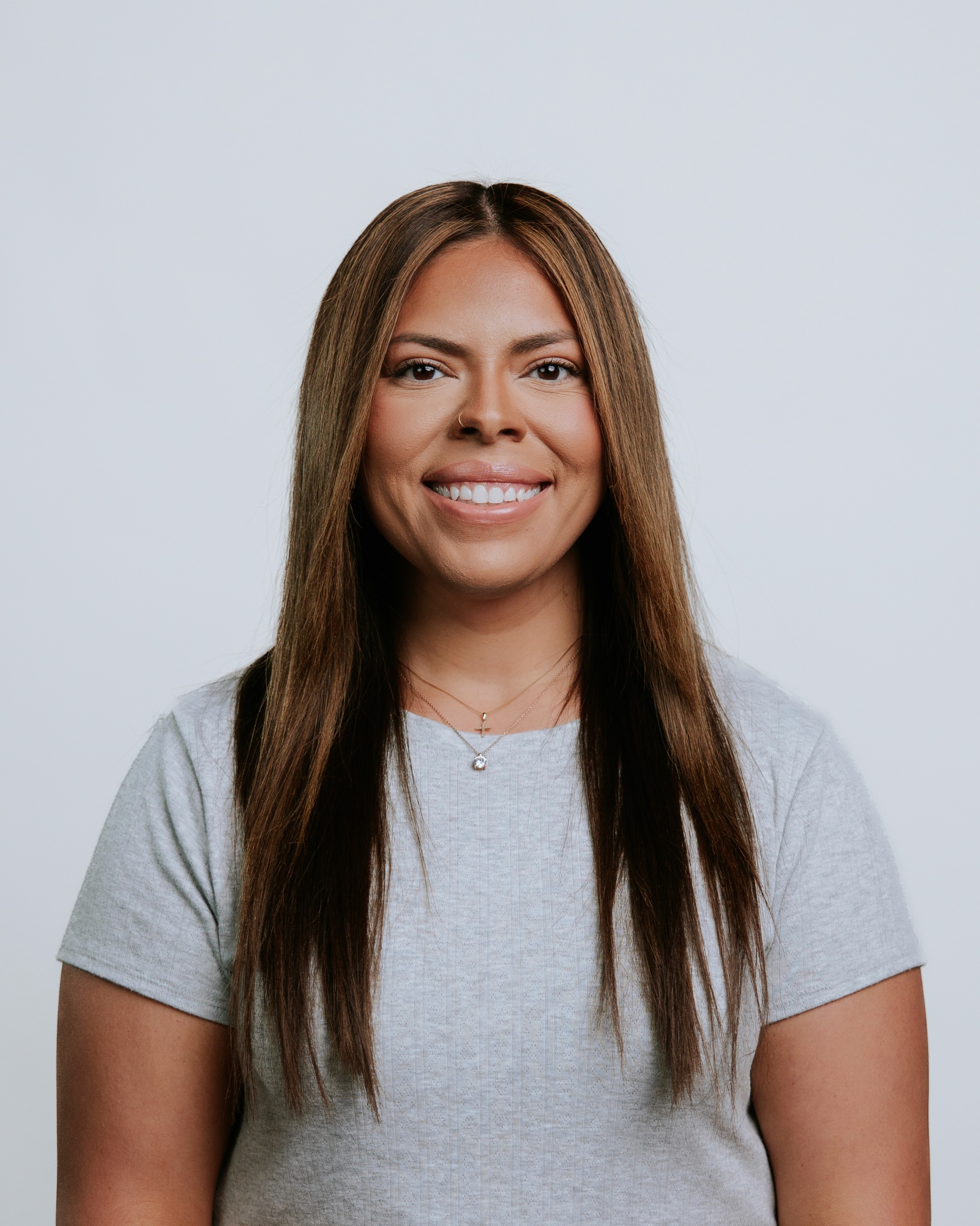 Smiling woman with long hair wearing an orange jacket against a light background.