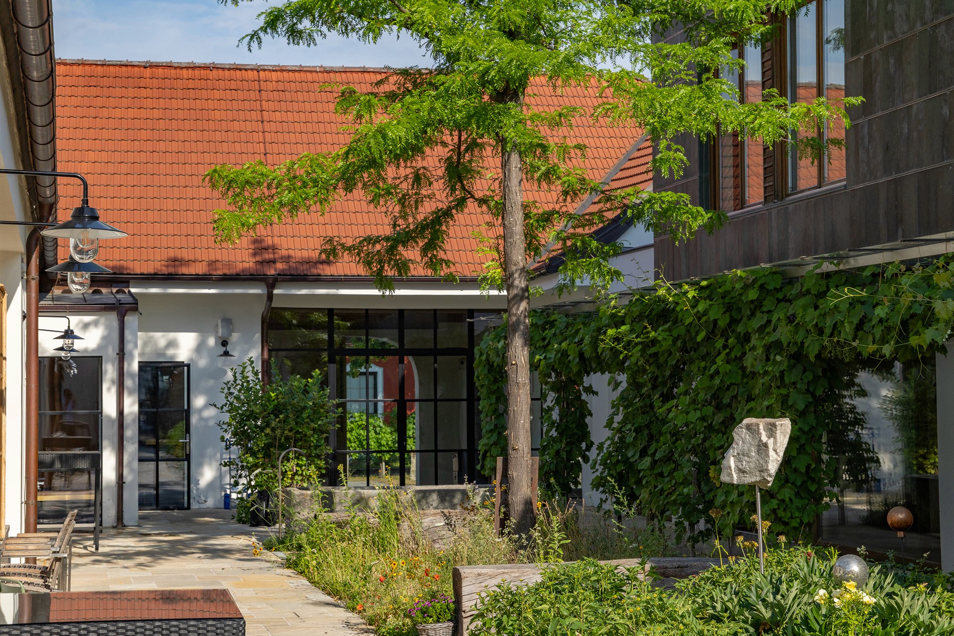 Besucherbereich mit Solitärbaum und naturnaher Wiesenbepflanzung in einem begrünten Innenhof.