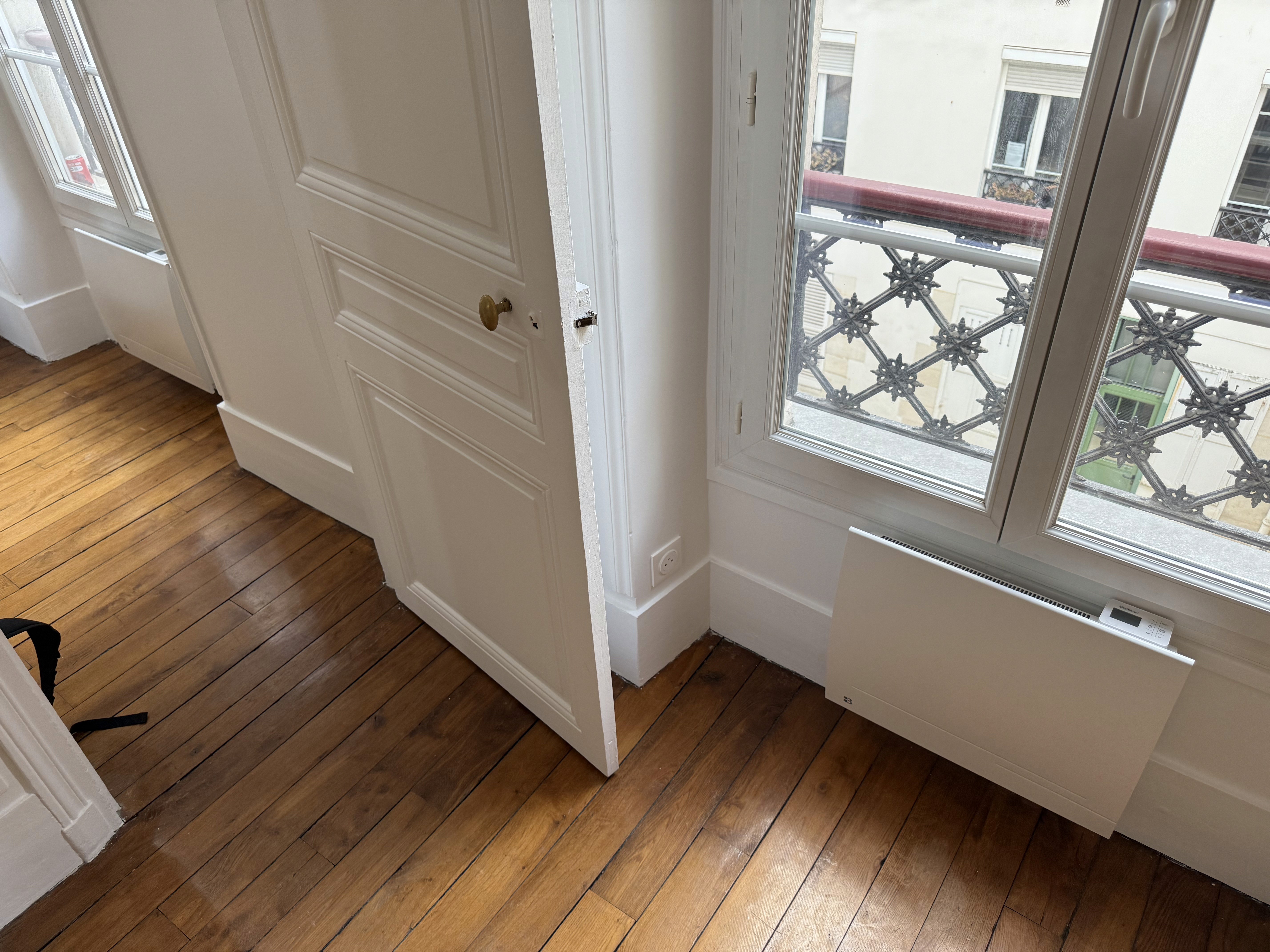 Rénovation d'appartement avec parquet ancien restauré, murs blancs et menuiserie traditionnelle élégante.