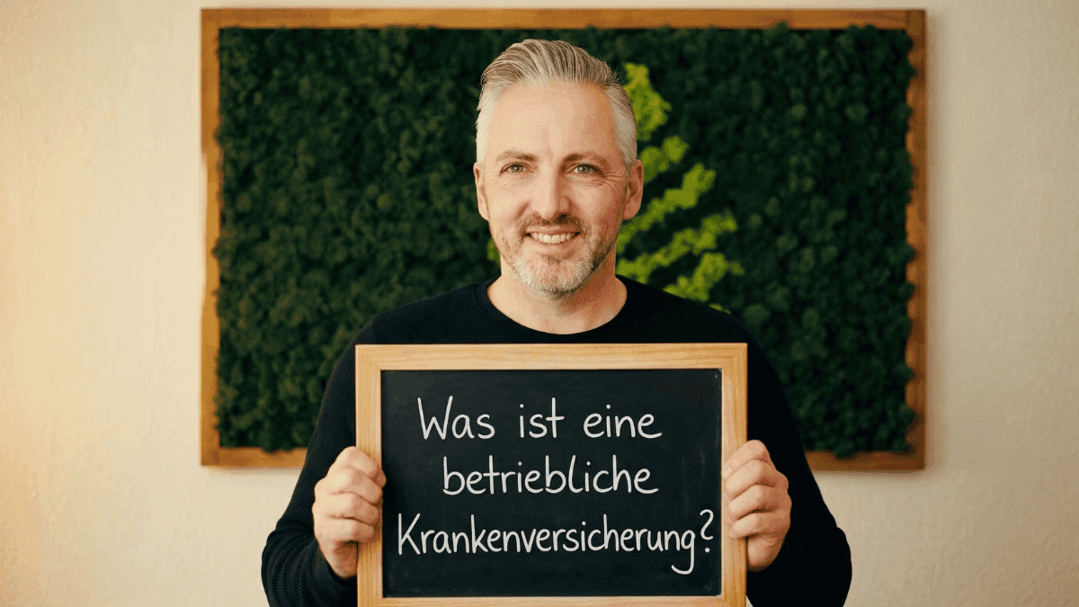Hannes Weindorf ist im Büro und hält ein Schild in der Hand, darauf steht: "Was ist eine betriebliche Krankenversicherung?"